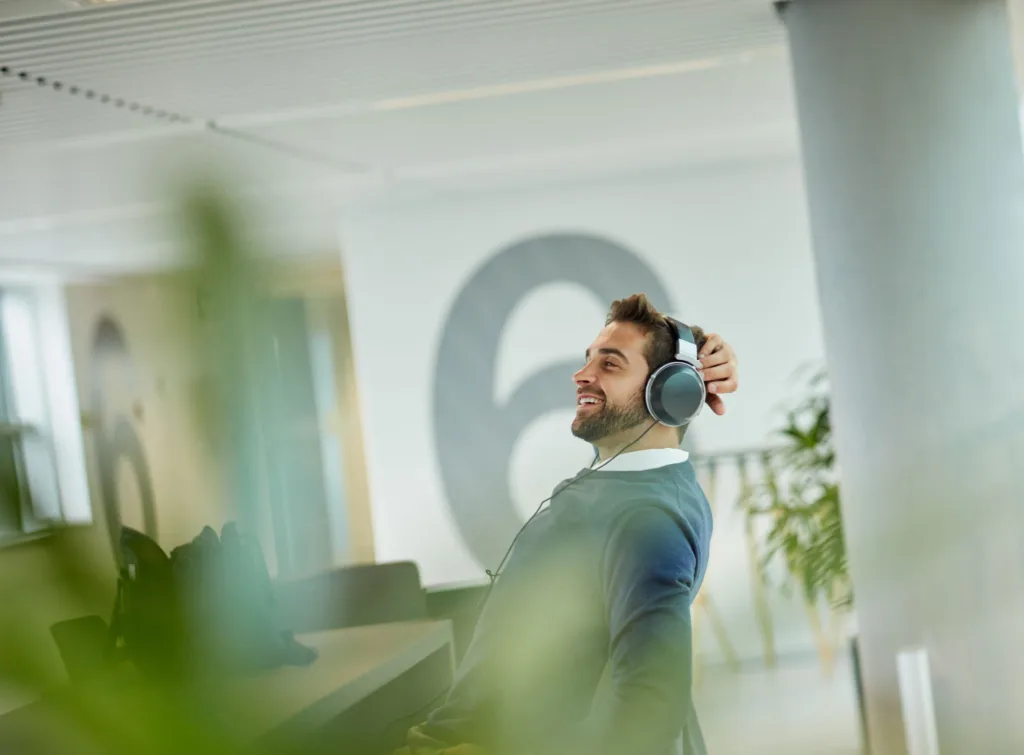 Man med hörlurar sitter vid ett skrivbord på ett kontor.