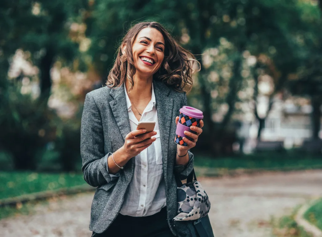 Kvinna med kaffemugg och mobiltelefon.